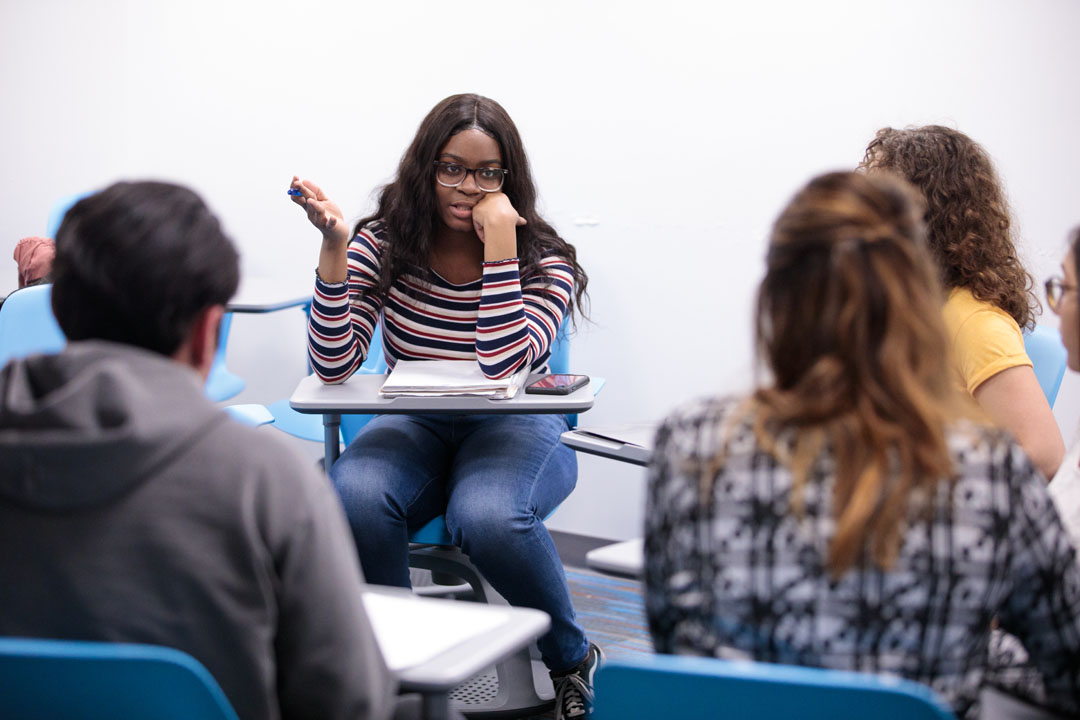 A student speaking to a circle of students in desks
