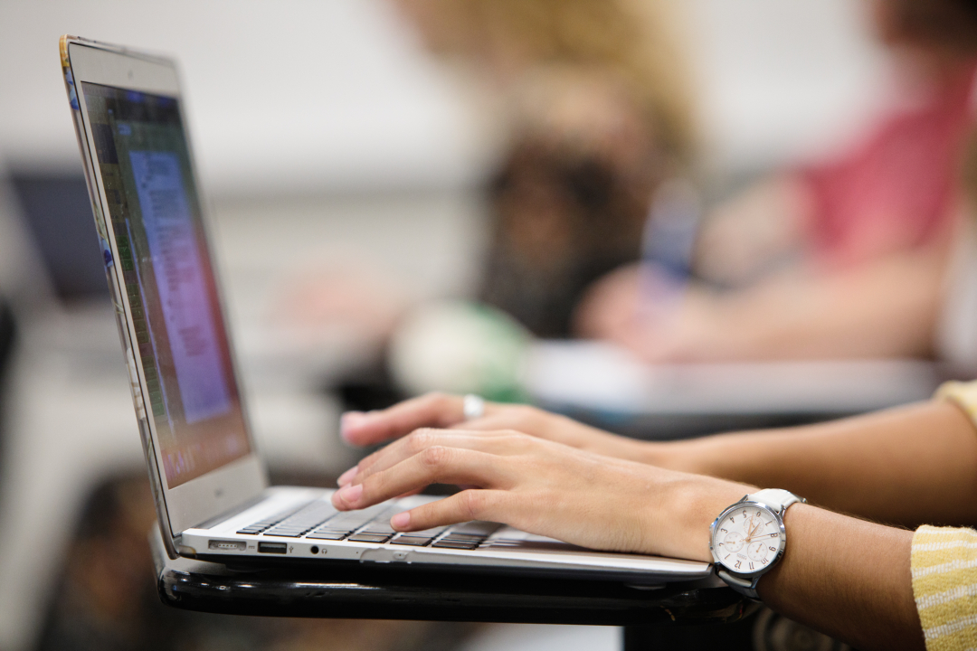 A close-up of a student's hands typing on a laptop